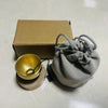 A small, light gray fabric pouch tied with twine rests next to a gold-colored singing bowl and a cardboard box.