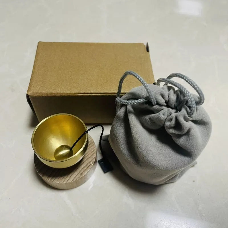 A small, light gray fabric pouch tied with twine rests next to a gold-colored singing bowl and a cardboard box.