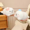 A person is holding two white seal plush toys, one with a pink hat and the other with a blue hat.