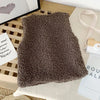 A dark brown plush fleece vest is displayed on a light surface next to some writing and a wooden object.