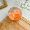 A clear, spherical stress ball filled with orange fruit slices resting on a wooden cutting board.