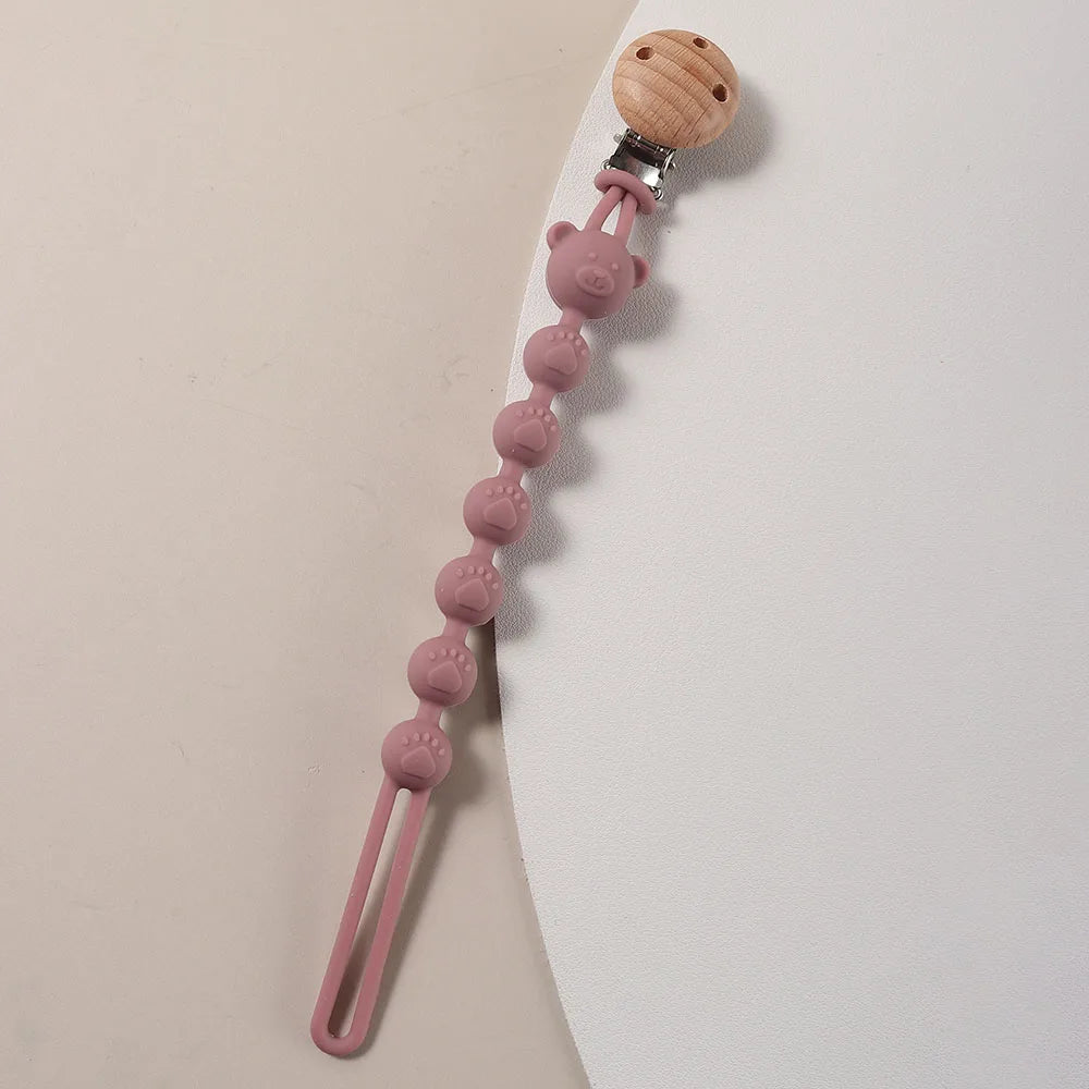 A silicone pacifier clip featuring a wooden bear paw top and a string of pink silicone beads.
