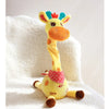 A yellow dancing talking giraffe plush toy with pink accents sitting on a white fluffy surface.