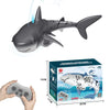 A gray shark toy is shown alongside its remote control and packaging box.