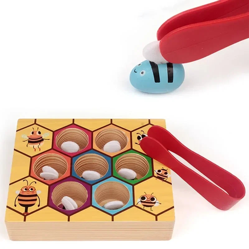 A red wooden bee trap toy with white clips is shown next to a yellow wooden game board featuring various bee-themed holes.