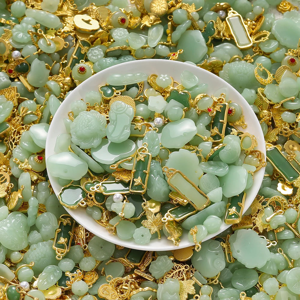 A pile of light green imitation jade charms and beads mixed with gold-colored jewelry findings on a white dish.