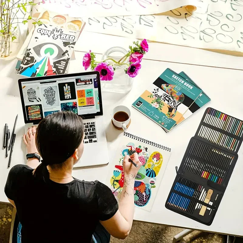 A person is sketching on a white table with various art supplies including a drawing book and a large set of colored pencils.