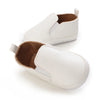 A pair of white baby first walker sneakers with a dinosaur print detail.
