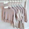A set of light pink knit sweater and pants for a toddler, displayed on a white rack.
