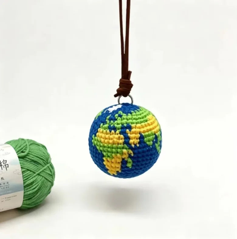 A handcrafted crochet globe charm with a blue and green design hanging from a brown leather cord.