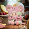 A pink and green fluffy bear plush charm with large ears and a bow, resting on a wooden surface.