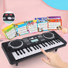 A black 37-key kids electronic keyboard with a microphone and colorful sheet music displayed on a pink background.