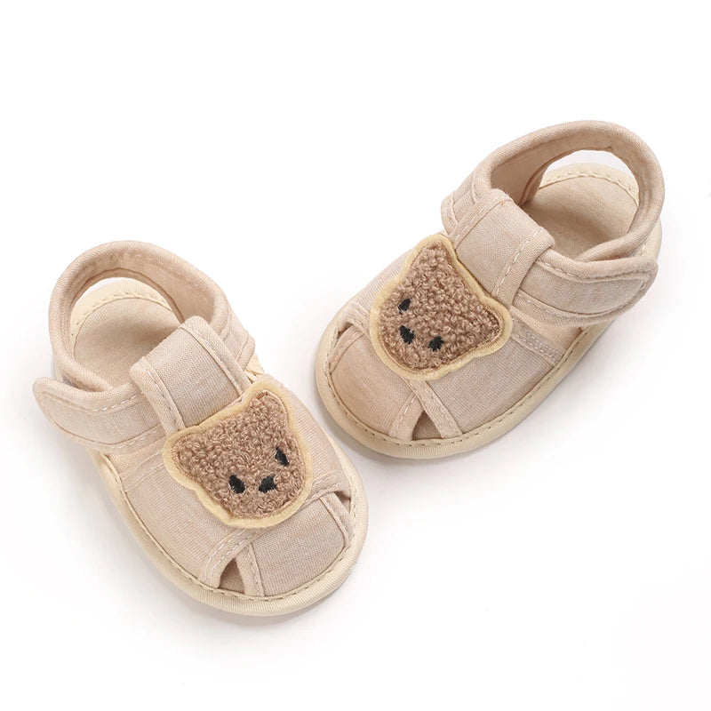 Pair of beige soft sole sandals for baby's first steps featuring a cute bear design