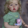 A realistic reborn baby doll with soft cloth body wearing a green dress and a light green headband.