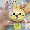 A hand holds a yellow squishy stress relief toy shaped like a cute, smiling face with large eyes and ears.