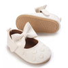 A pair of white lace-trimmed baby girl moccasin shoes with a bow and a tan sole.
