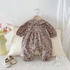 A floral doll collar baby girl long sleeve jumpsuit is displayed on a white surface with a light colored pillow.