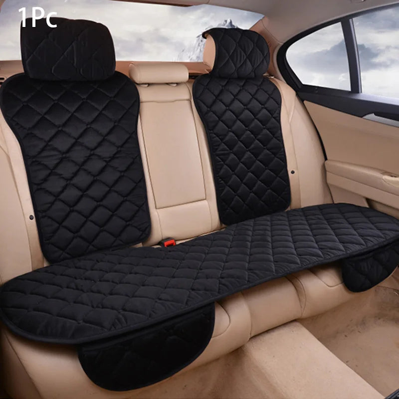 A black car seat protector with a quilted pattern is shown installed in the back seat of a vehicle.