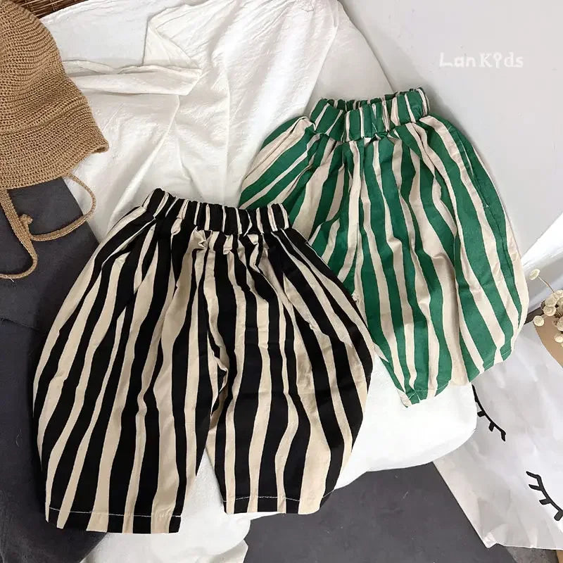 A pair of black and beige striped cotton harem pants for kids laid out on a white surface.