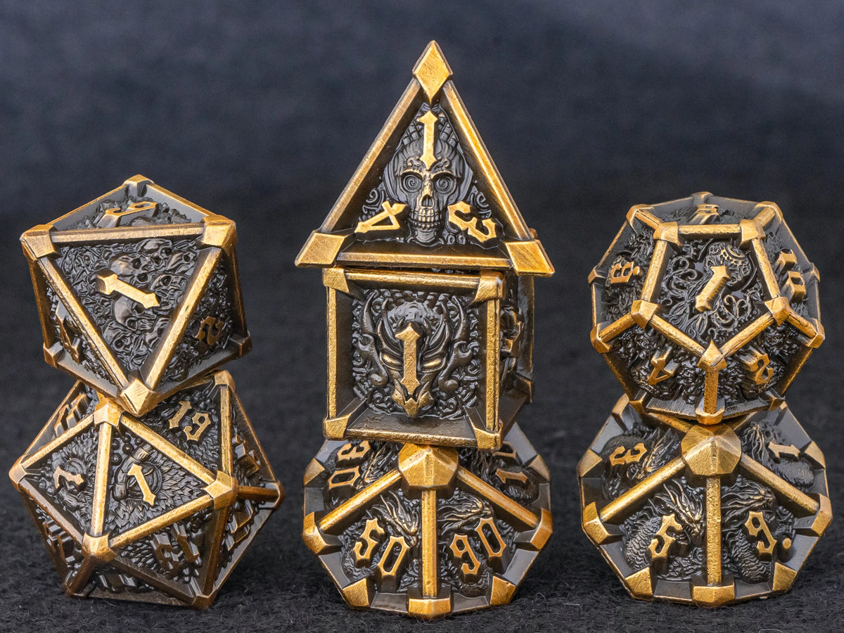 A set of seven metal dice featuring a skull and dragon design in gold and dark metal tones.