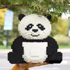 A white and black panda 3D model made of building blocks is held outdoors under green foliage.