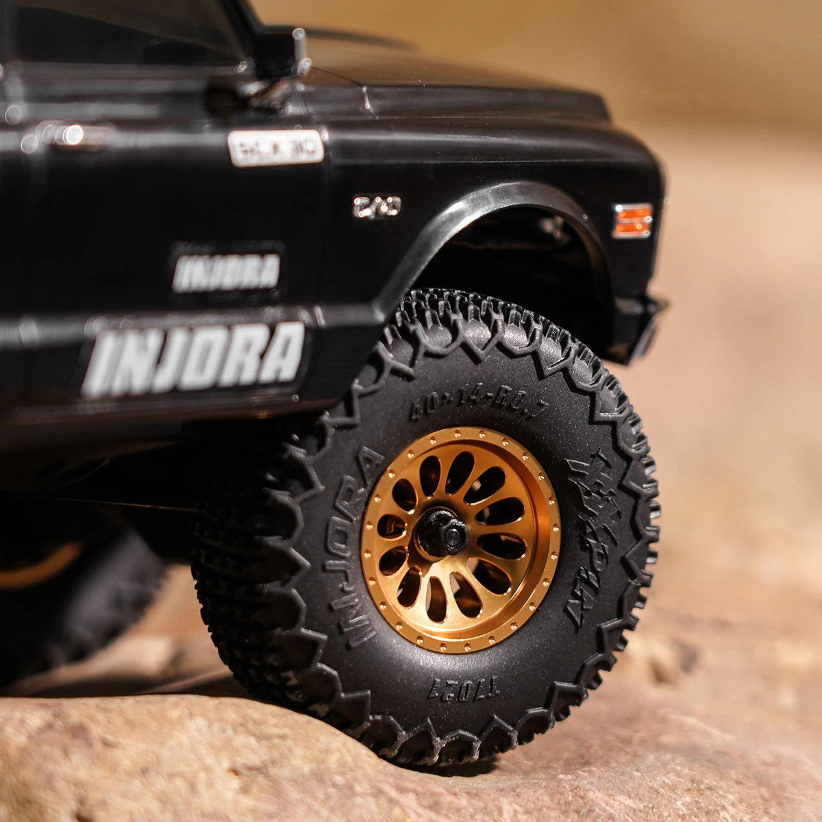 Black RC truck with Injora branding and a large black beadlock tire on a wooden surface.