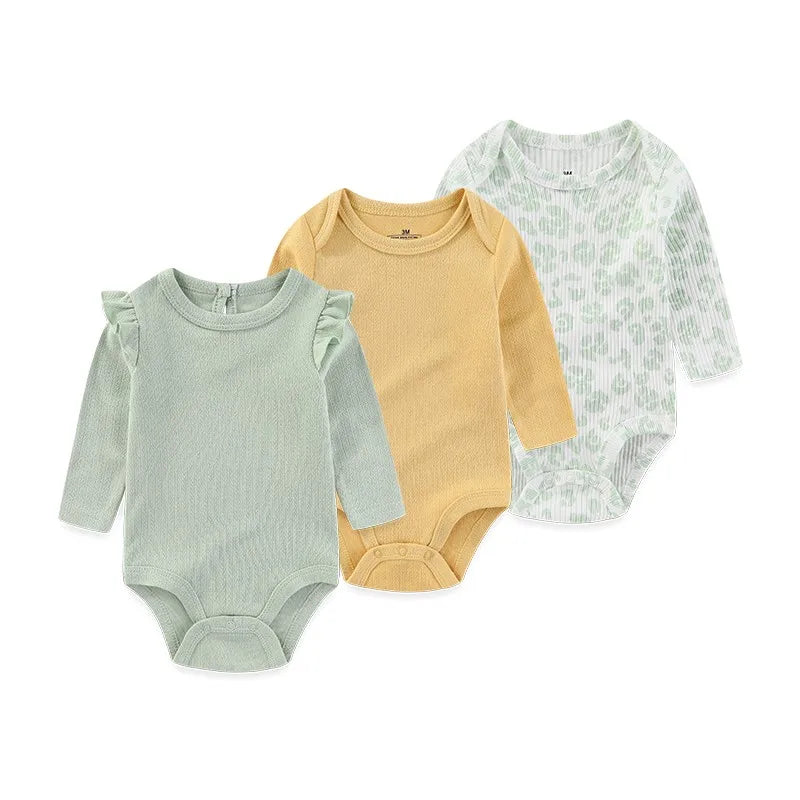 A set of three long-sleeved cotton baby bodysuits in light green, yellow, and white patterned fabric.