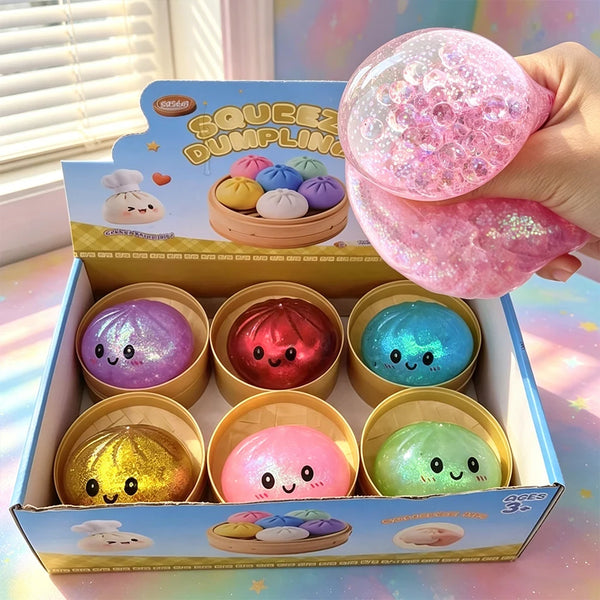 A box of pink and blue glitter dumpling squishies is shown with a hand holding one of the pink ones.