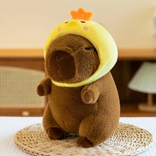 A brown capybara plush toy wearing a yellow hood, sitting on a woven mat.