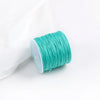A roll of teal green cotton nylon macrame cord for jewelry making and crafts is shown next to a white cloth.