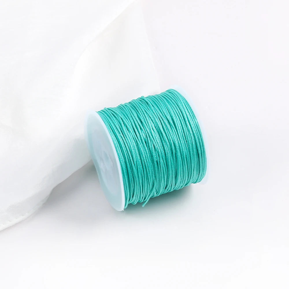 A roll of teal green cotton nylon macrame cord for jewelry making and crafts is shown next to a white cloth.