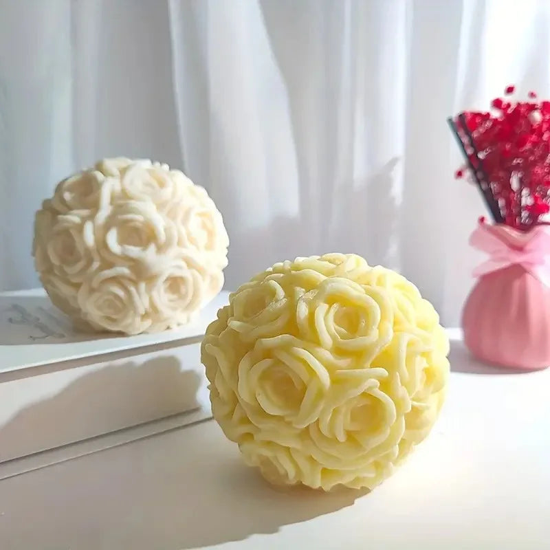A yellow rose flower ball made of silicone is displayed on a white surface next to a pink vase with red flowers.