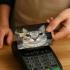 A hand holds a card featuring a cat face meme, placed on a black electronic device.