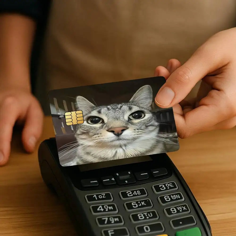 A hand holds a card featuring a cat face meme, placed on a black electronic device.