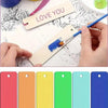 Hands are painting a wooden bookmark with blue paint on a textured surface.