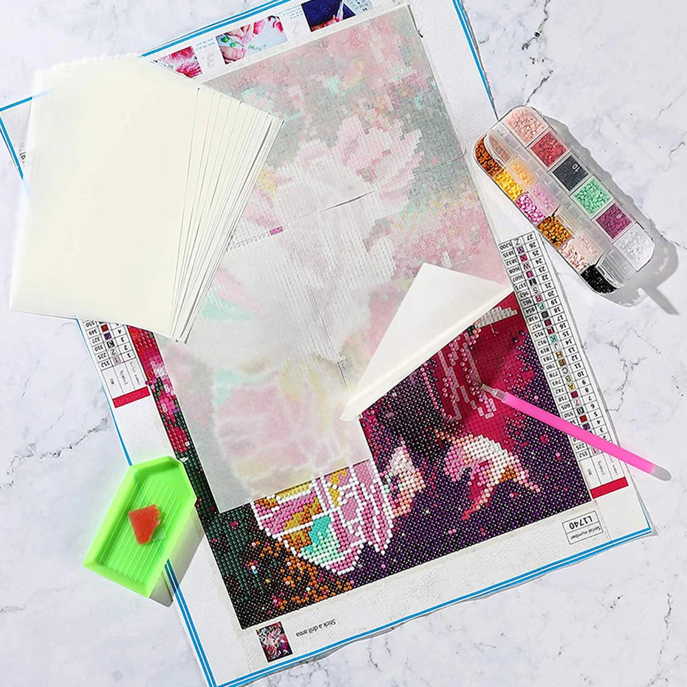A sheet of double-sided non-stick release paper for diamond painting is shown next to a palette of colorful beads and a ruler