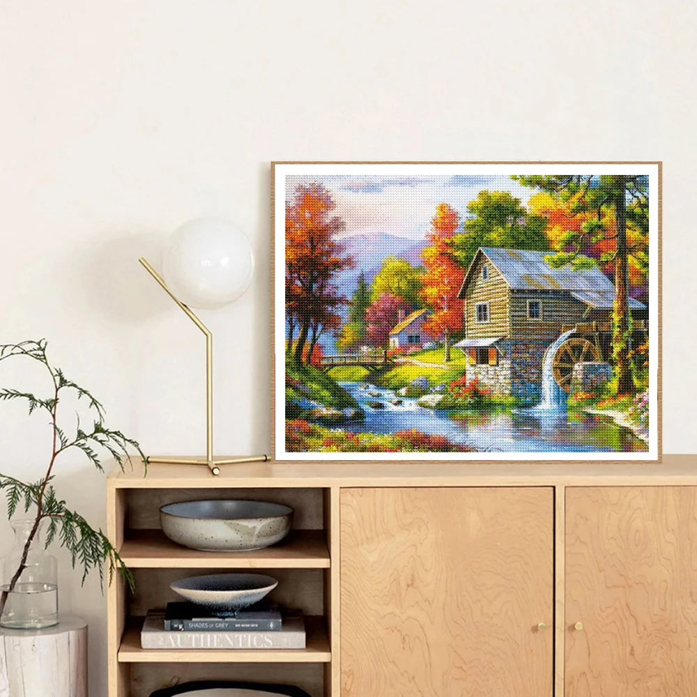 Diamond painting kit featuring a scenic forest house with autumn foliage and flowing water.