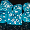 A close-up of bright blue polyhedral dice with white numbering and gold accents, reflecting on a dark surface.