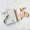 A set of silicone baby-themed cake molds including a stroller, bottle, and pacifier on a white plate.