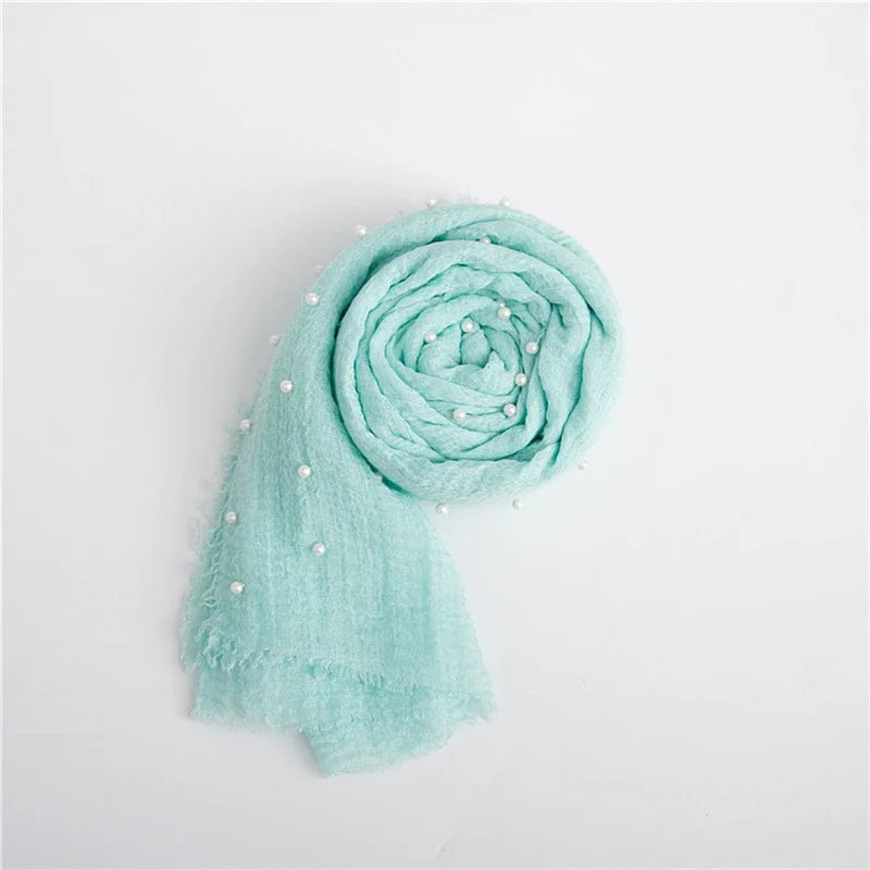 Light mint green knit wrap with a pearl headband, rolled and draped on a white background.