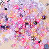 A colorful mix of iridescent resin and rhinestone pearls in pink, purple, and gold shades for crafts and nail art.