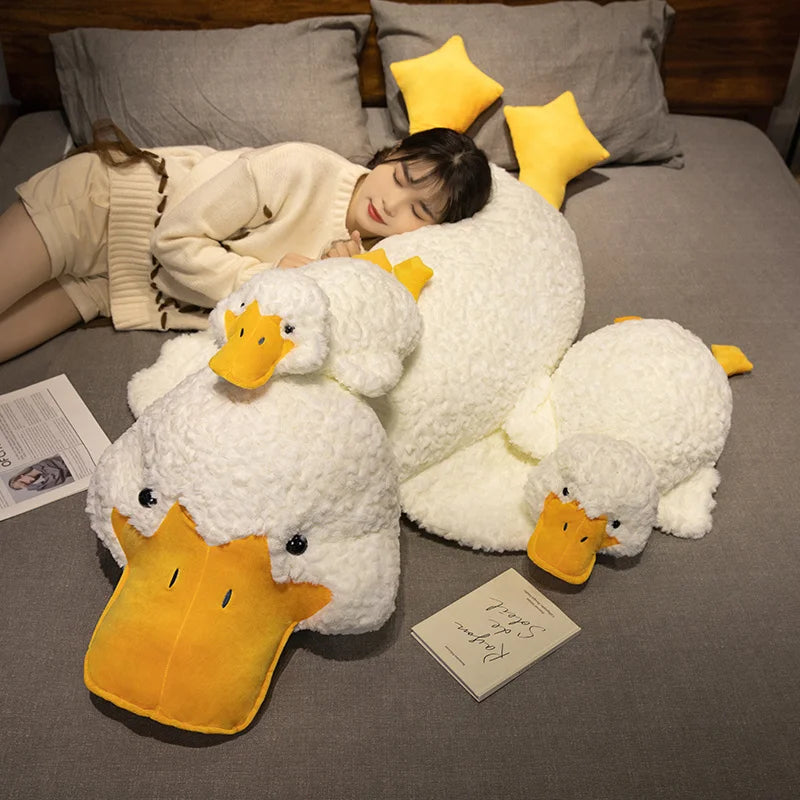 A person is relaxing on a gray couch with a giant white plush duck pillow and yellow star pillows.