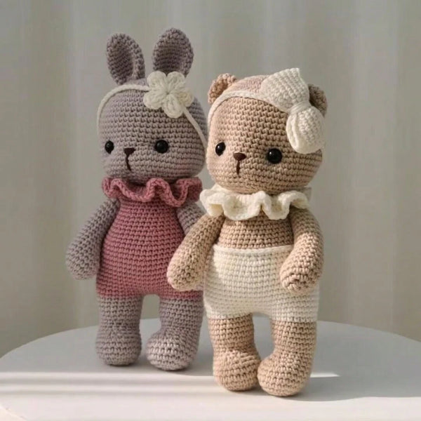 Et par håndlagde heklede plushdyr, en kanin og en bjørn, i rosa og kremfarger.