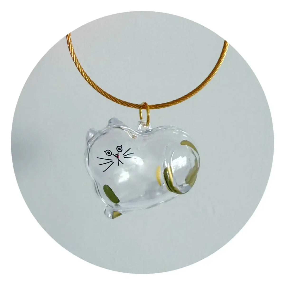 A clear glass charm shaped like a cat is suspended from a gold-colored cord.