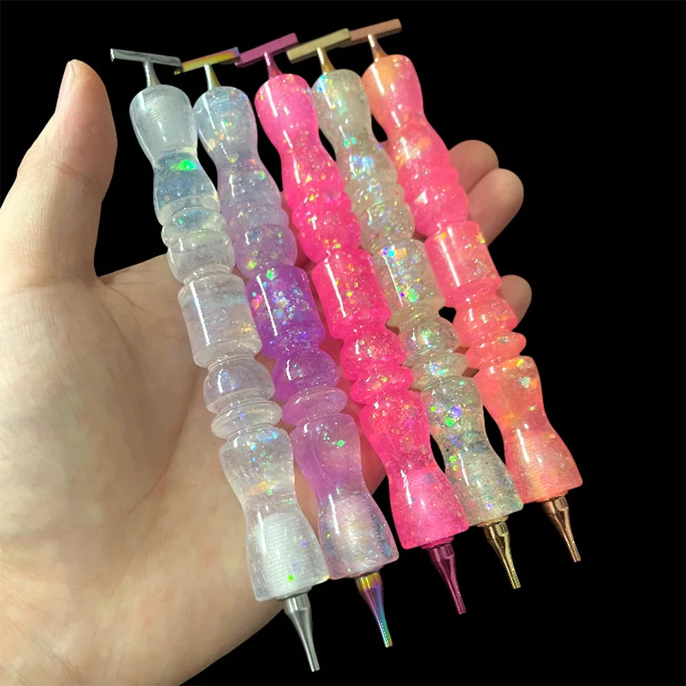 A hand holds a set of glitter resin diamond painting pens with colorful, wavy handles.