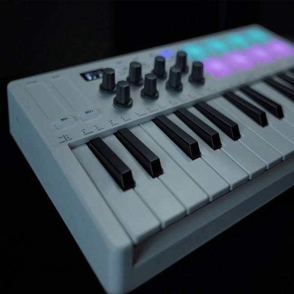 A white portable MIDI keyboard controller with black keys and illuminated pads is shown from above.