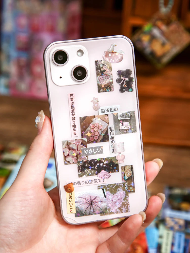 A hand holds a phone case decorated with various Japanese vintage kawaii stickers for scrapbooking