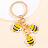 Gold-toned keychain featuring enamel bees and a daisy design.