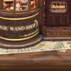 A wooden miniature kit of a magic wand shop with a door and a sign, displayed on a wooden surface.