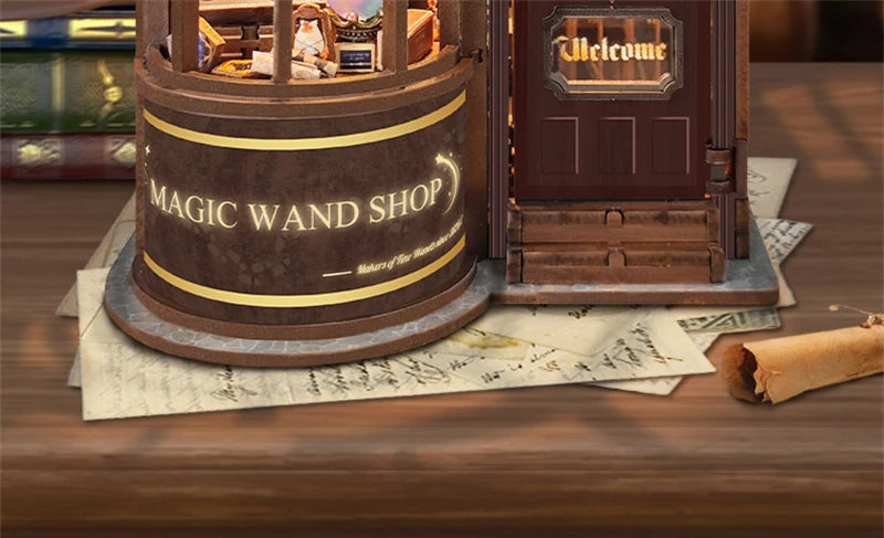 A wooden miniature kit of a magic wand shop with a door and a sign, displayed on a wooden surface.